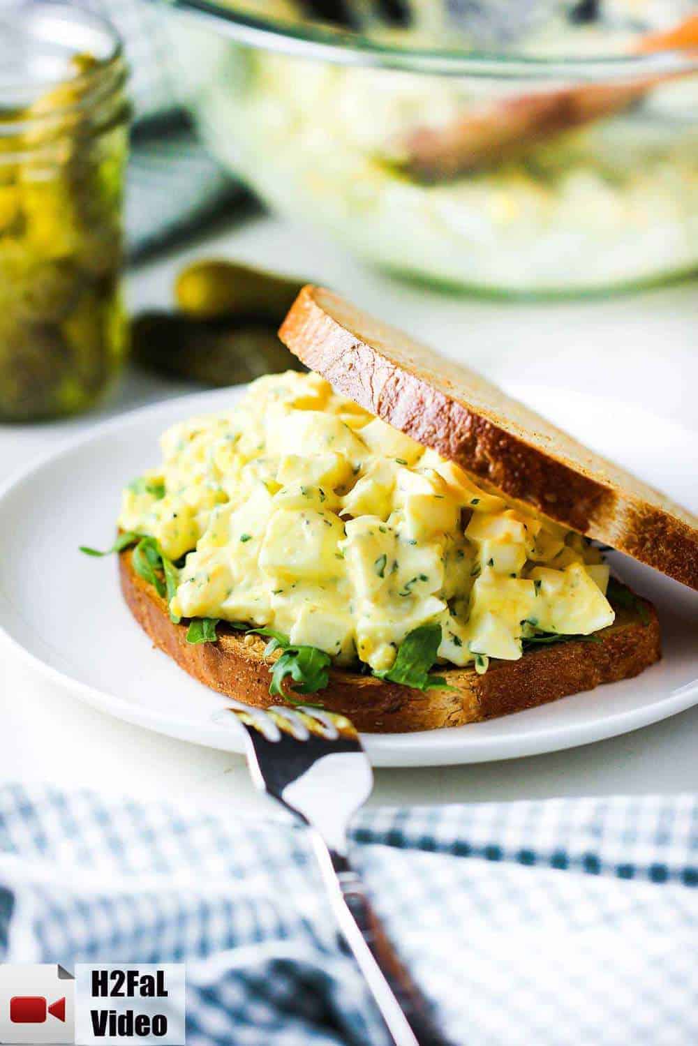 Best-ever egg salad on a white plate with pickles nearby