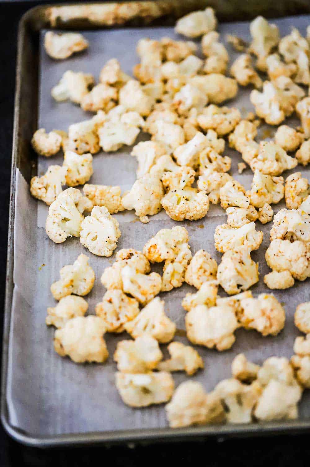 Seasoned cauliflower florets resting on a large baking sheet lined with parchment paper. 