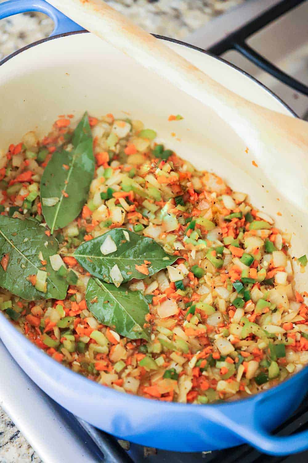 A large Dutch oven filled with sautéed mirepoix and bay leaves. 