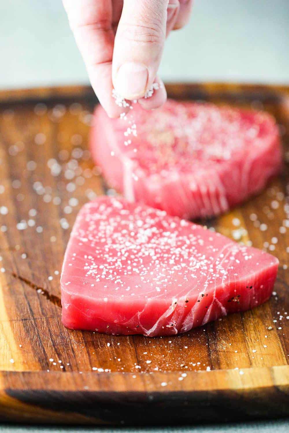 Salt being sprinkled onto tuna steaks for Mediterranean tuna steaks