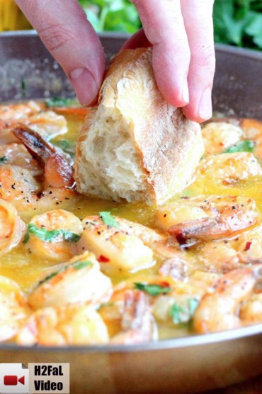A hand dipping bread into succulent shrimp scampi