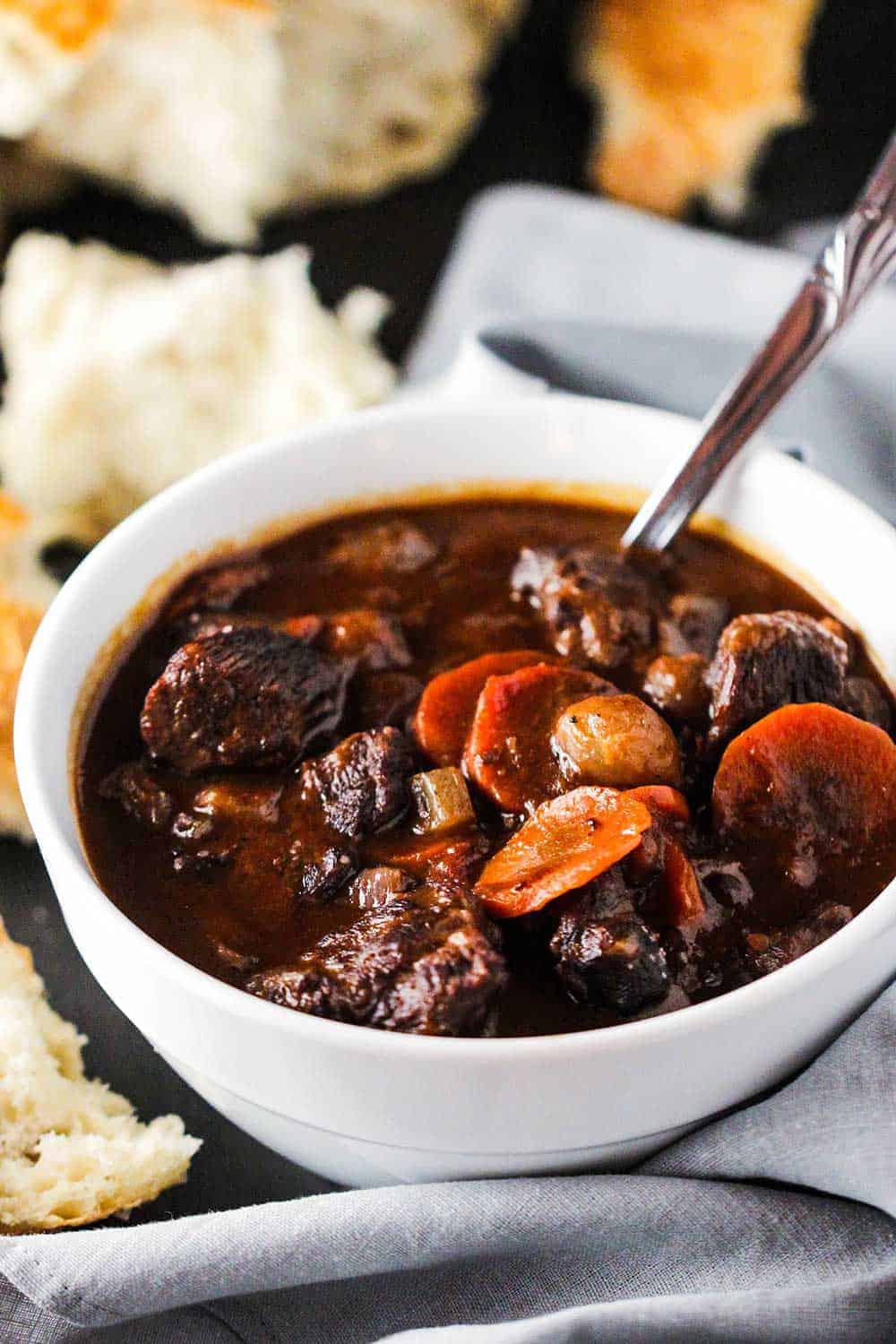 A white bowl filled with hearty beef stew next to torn white bread. 