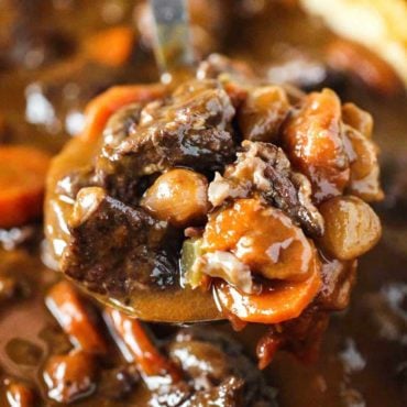 A ladle filled with hearty beef stew over a Dutch oven of the stew.