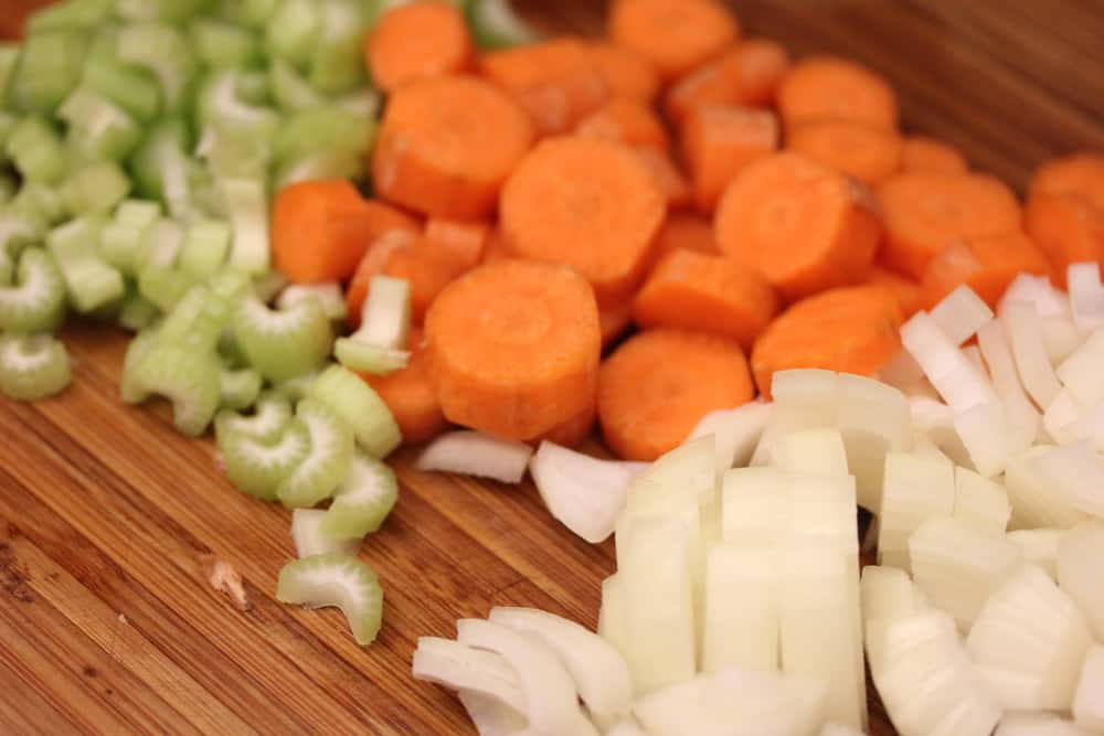 A wooden cutting board topped with sliced celery, carrots, and onion. 