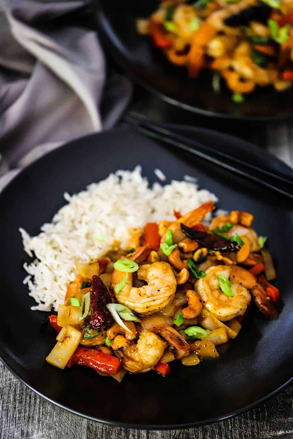 A black individual dinner plate with cooked Jasmine rice on one side and a serving of Kung Pao Shrimp on the other side. 