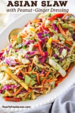 A close-up view of an Asian slaw with Peanut Ginger Dressing on a white platter with a golden serving spoon inserted into the side.