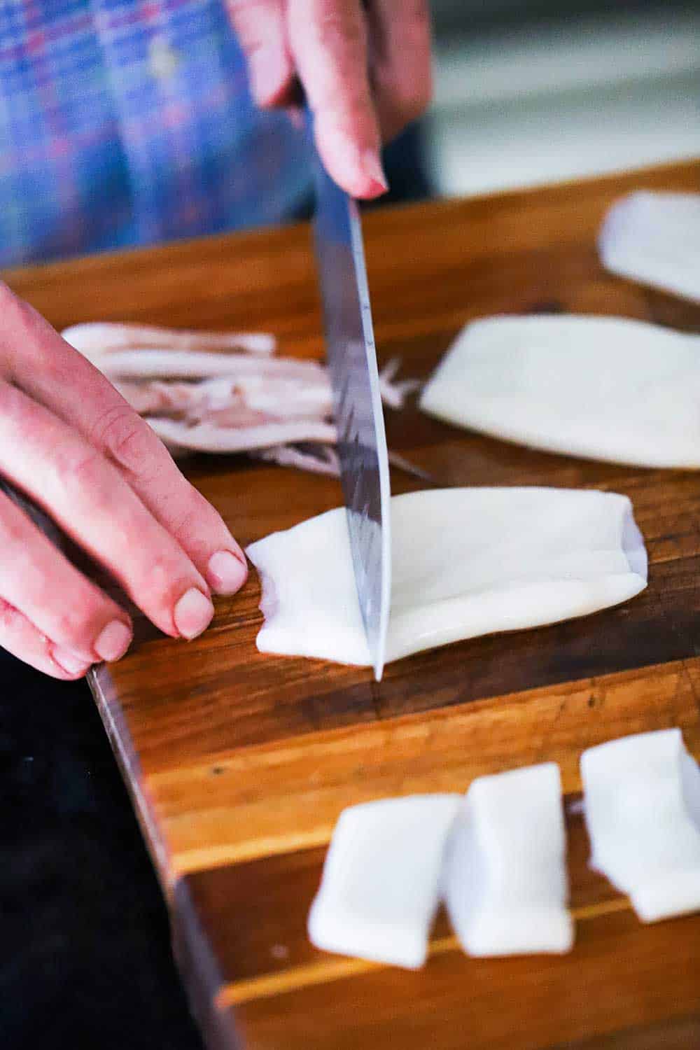 A person using a chef's knife to slice squid tube into small ringlets on a cutting board. 