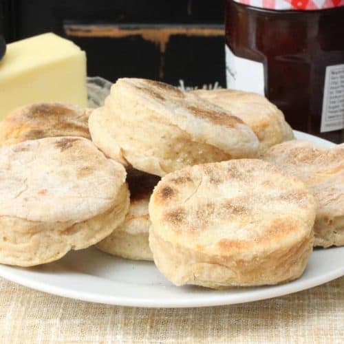 A plate full of homemade English muffins next to stick of butter.