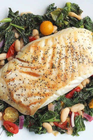Halibut with braised kale, beans & tomatoes on a white plate