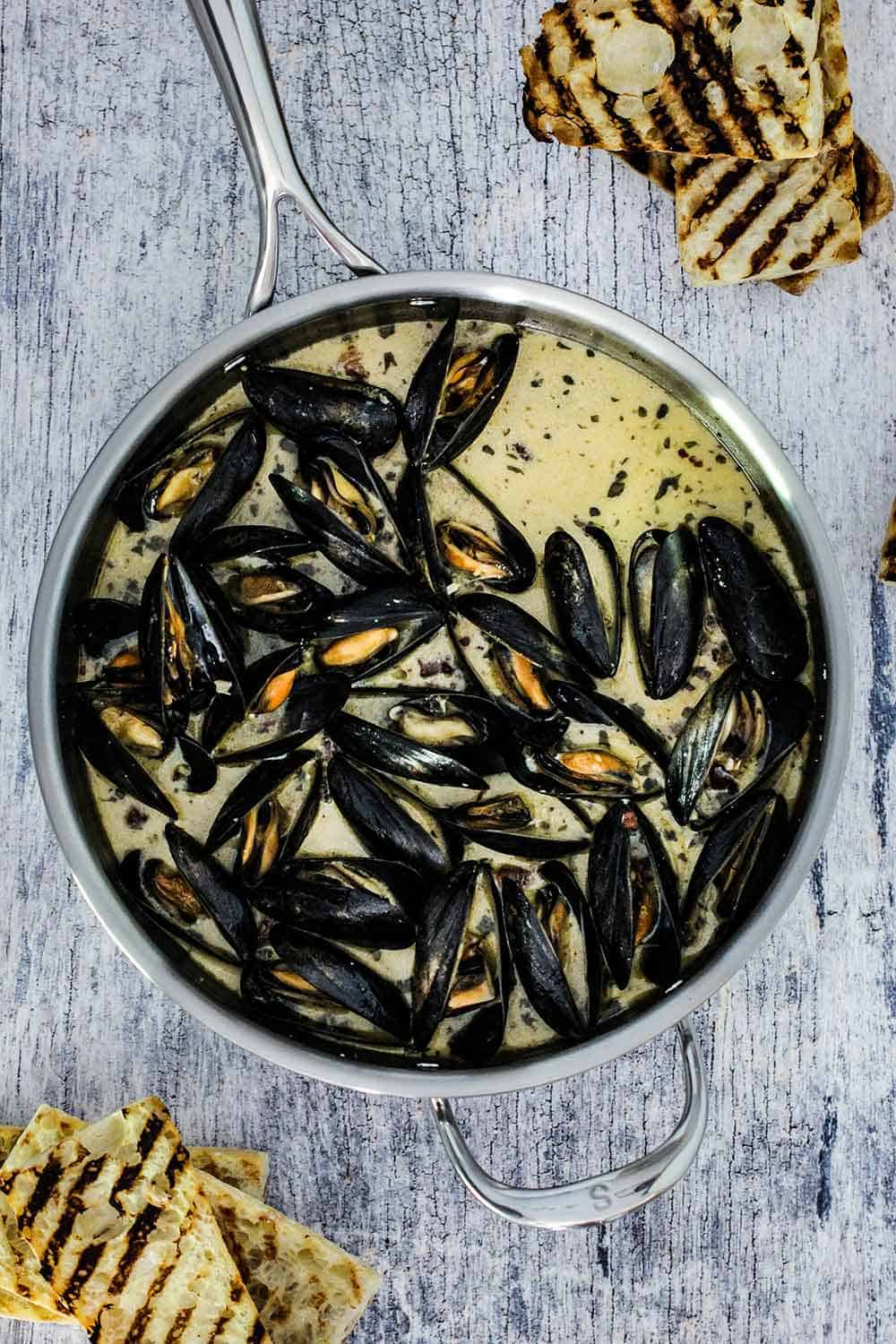 A large saucepan filled with steamed mussels with garlic and wine sauce. 