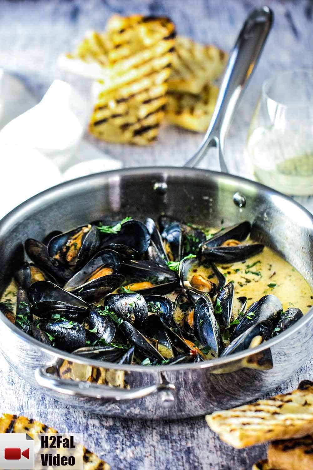 A large silver sauce pan with mussels and garlic and wine in it 