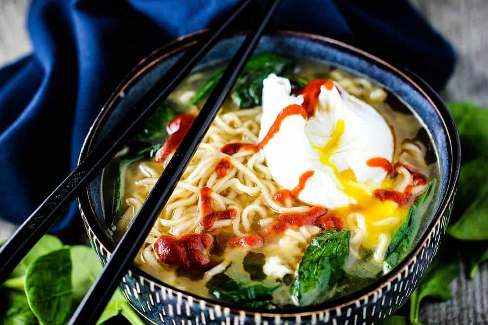 Zuppa di noodle ramen agli spinaci con uovo in camicia in una ciotola blu con bastoncini