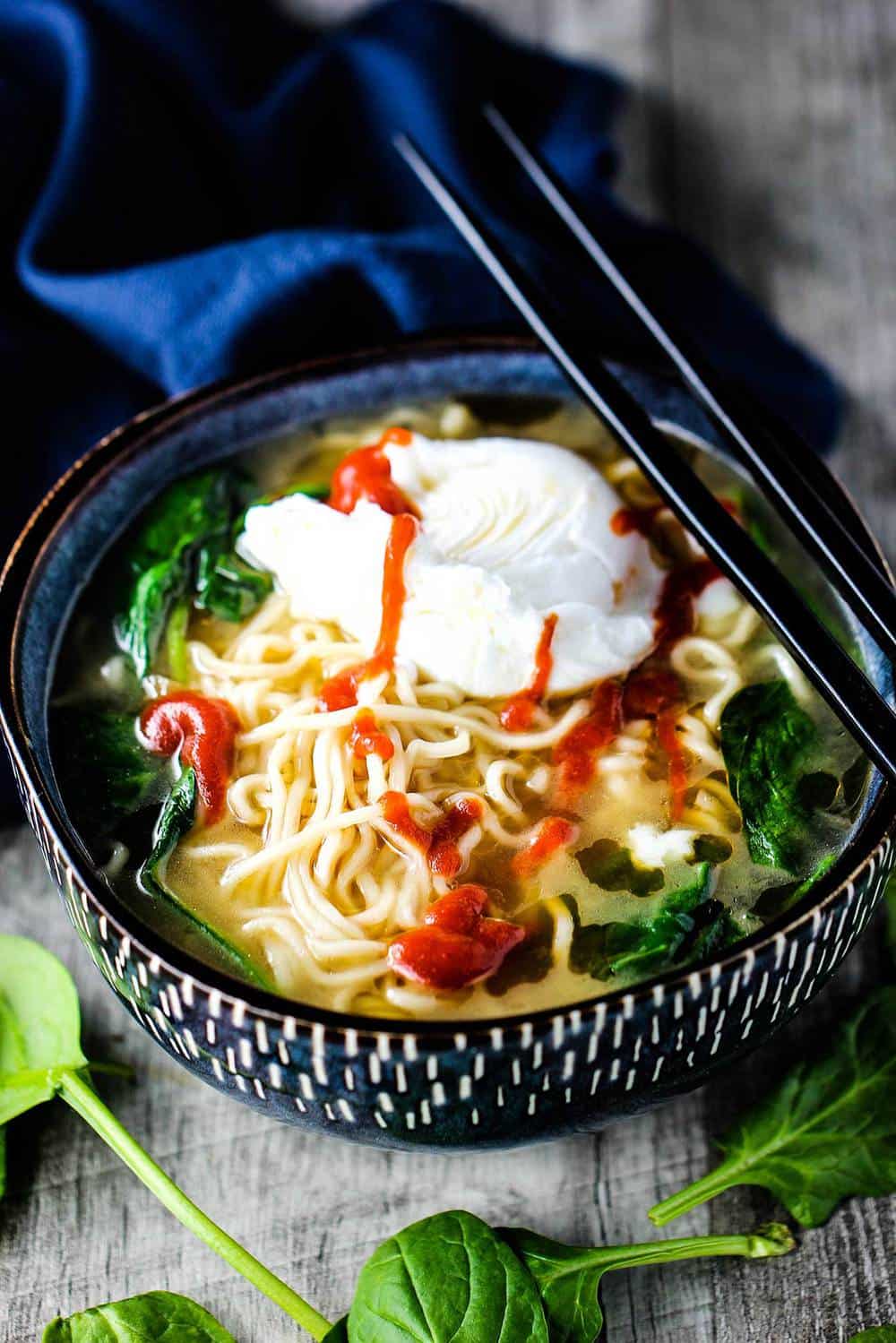 Soupe ramen aux épinards avec œuf poché dans un bol avec des baguettes sur le dessus