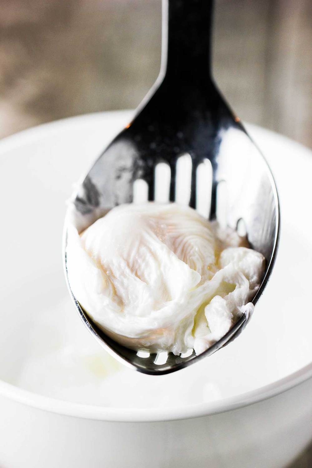 œuf poché dans une cuillère à rainures pour une soupe ramen nouilles aux épinards