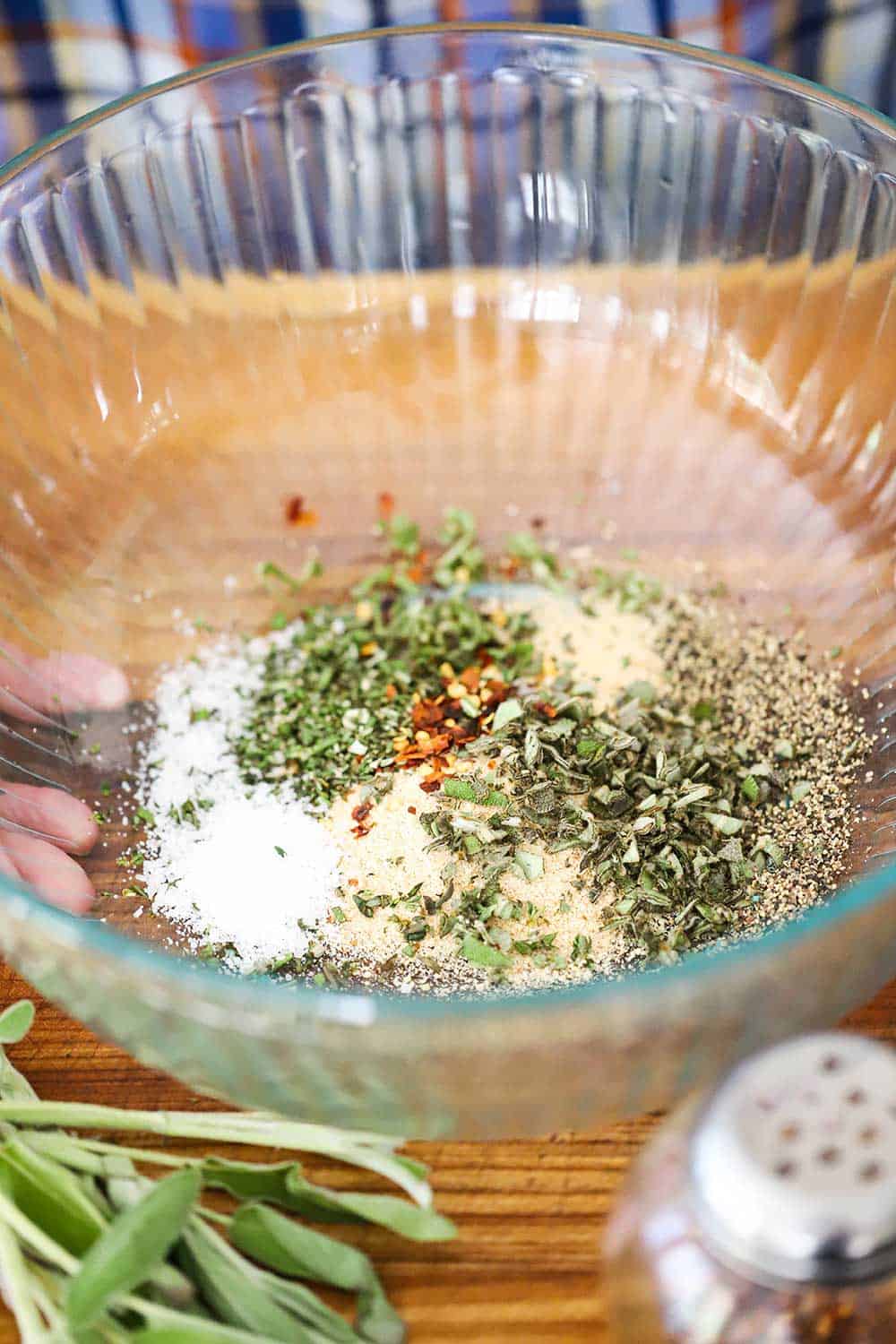 A large glass bowl filled with bread crumbs, fresh herbs, red pepper flakes, salt, and pepper. 