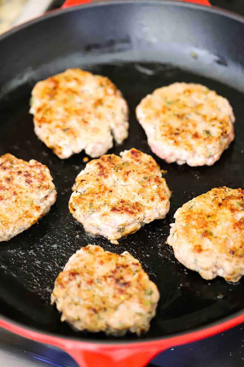 A large black skillet with orange exterior filled with 5 cooked maple sausage patties. 