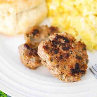 A close-up view of two maple sausage patties on a white plate with scrambled eggs and a biscuit.