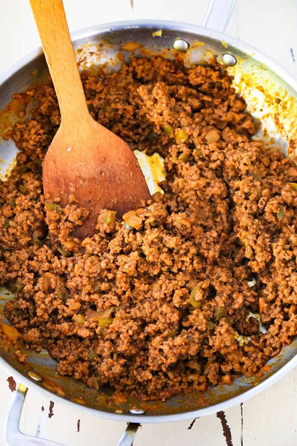 An overhead view of a skillet filled with sloppy joes meat mixture with a wooden spoon in the middle. 