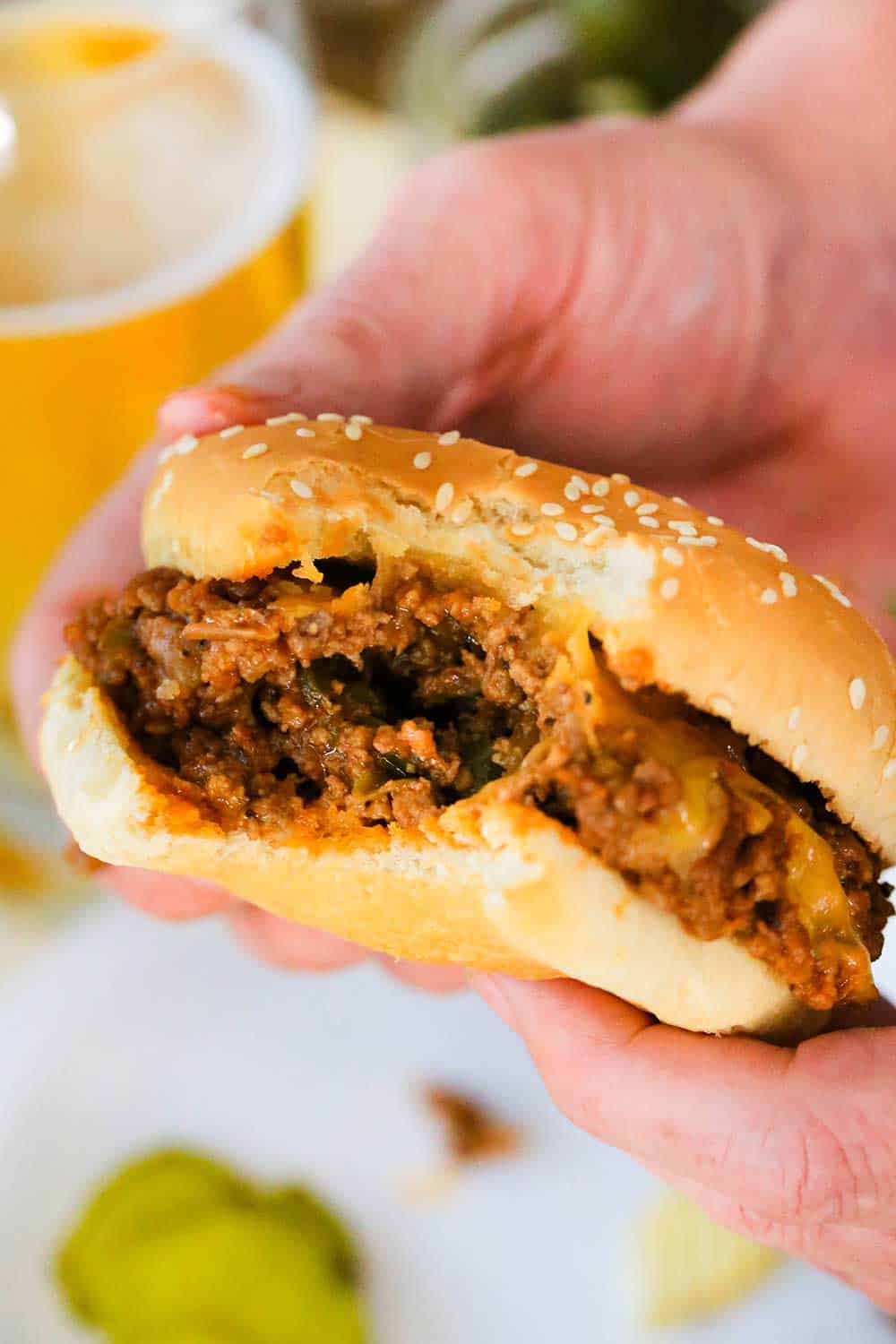 Two hands holding a sloppy joe sandwich with a bite taken out of it. 