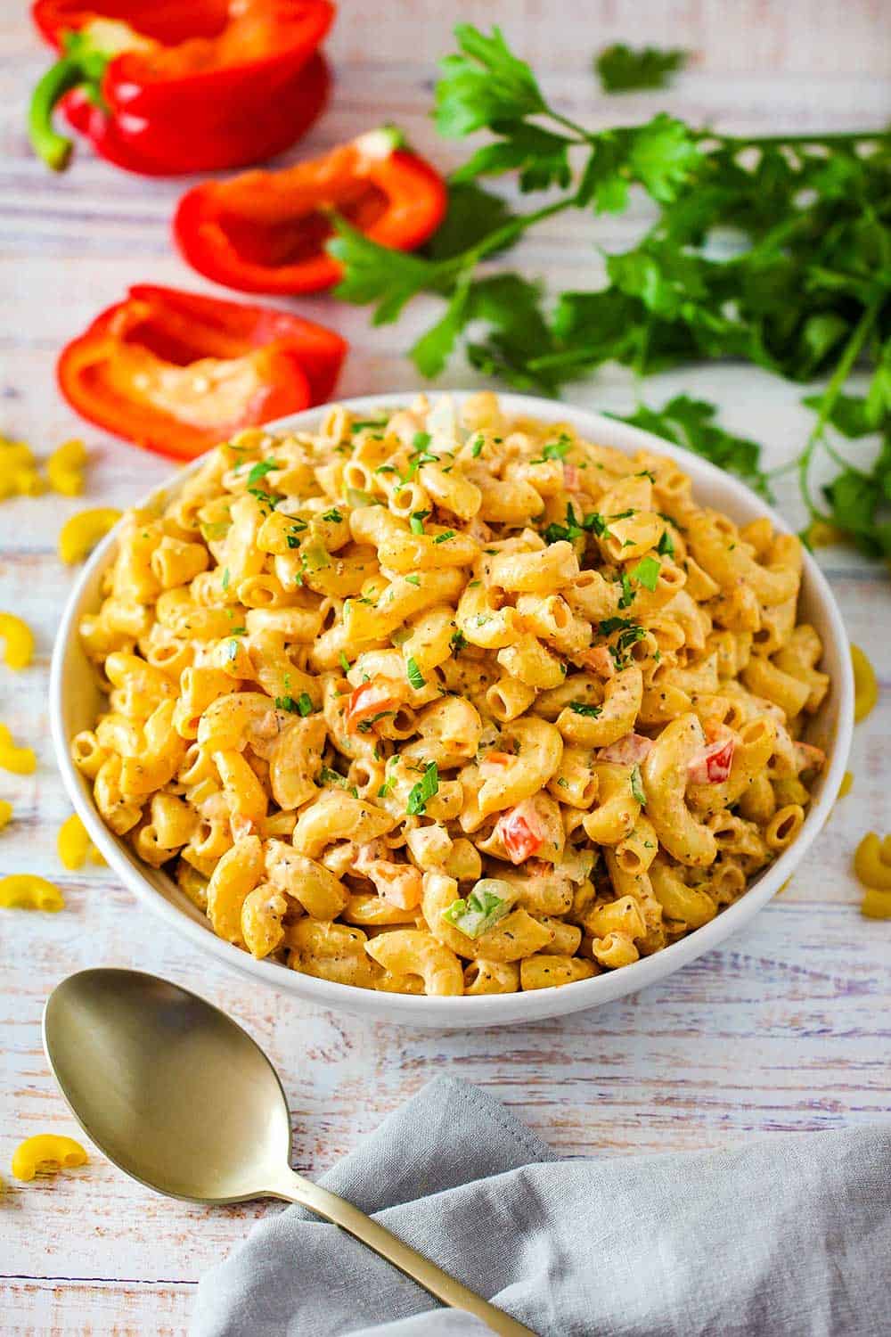 A white bowl full of Cajun pasta salad with a gold spoon nearby. 