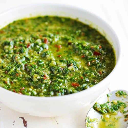 A white bowl of freshly made chimichurri sauce next to a spoon.