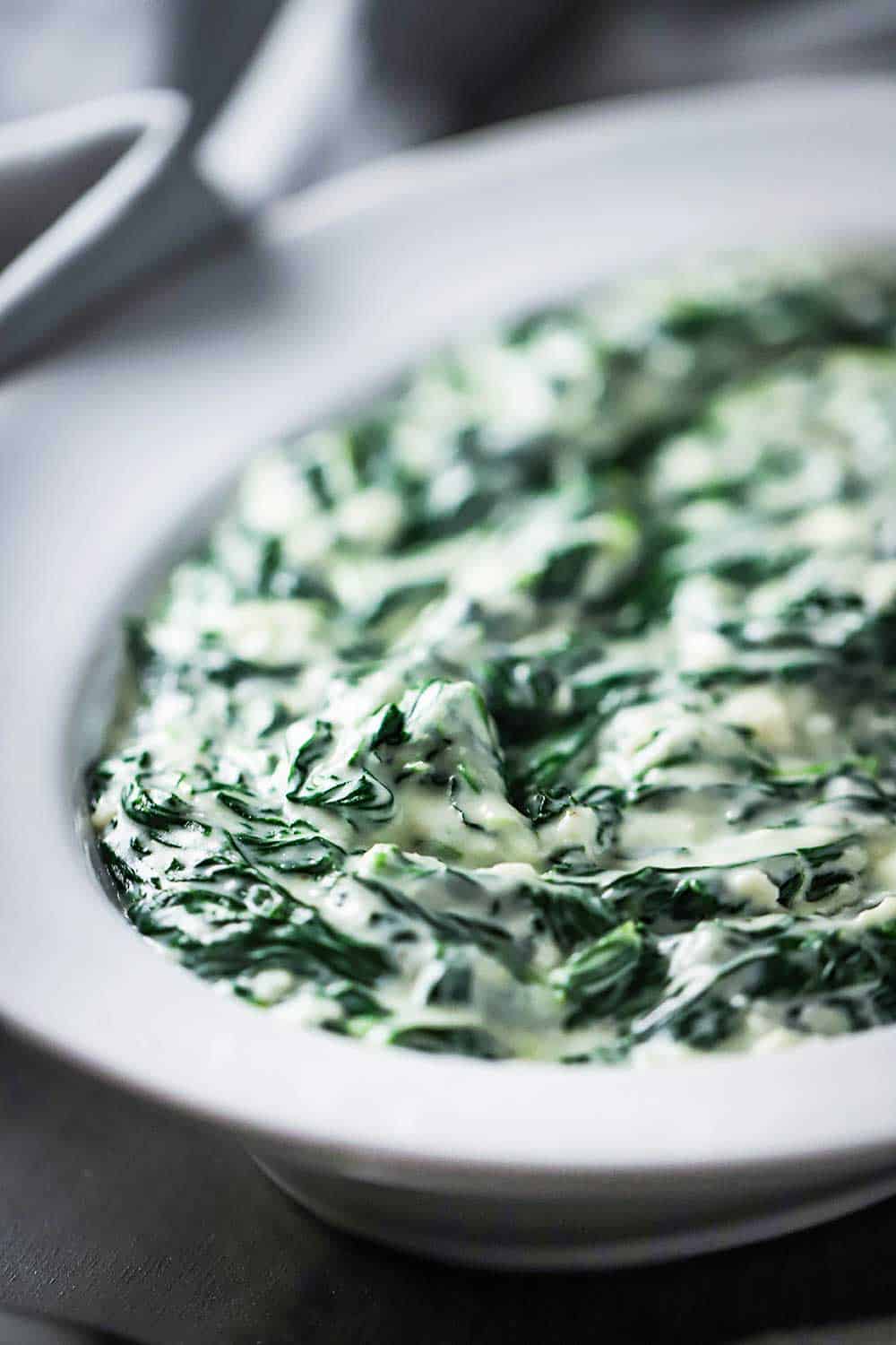 A white oval serving bowl filled with creamed spinach. 