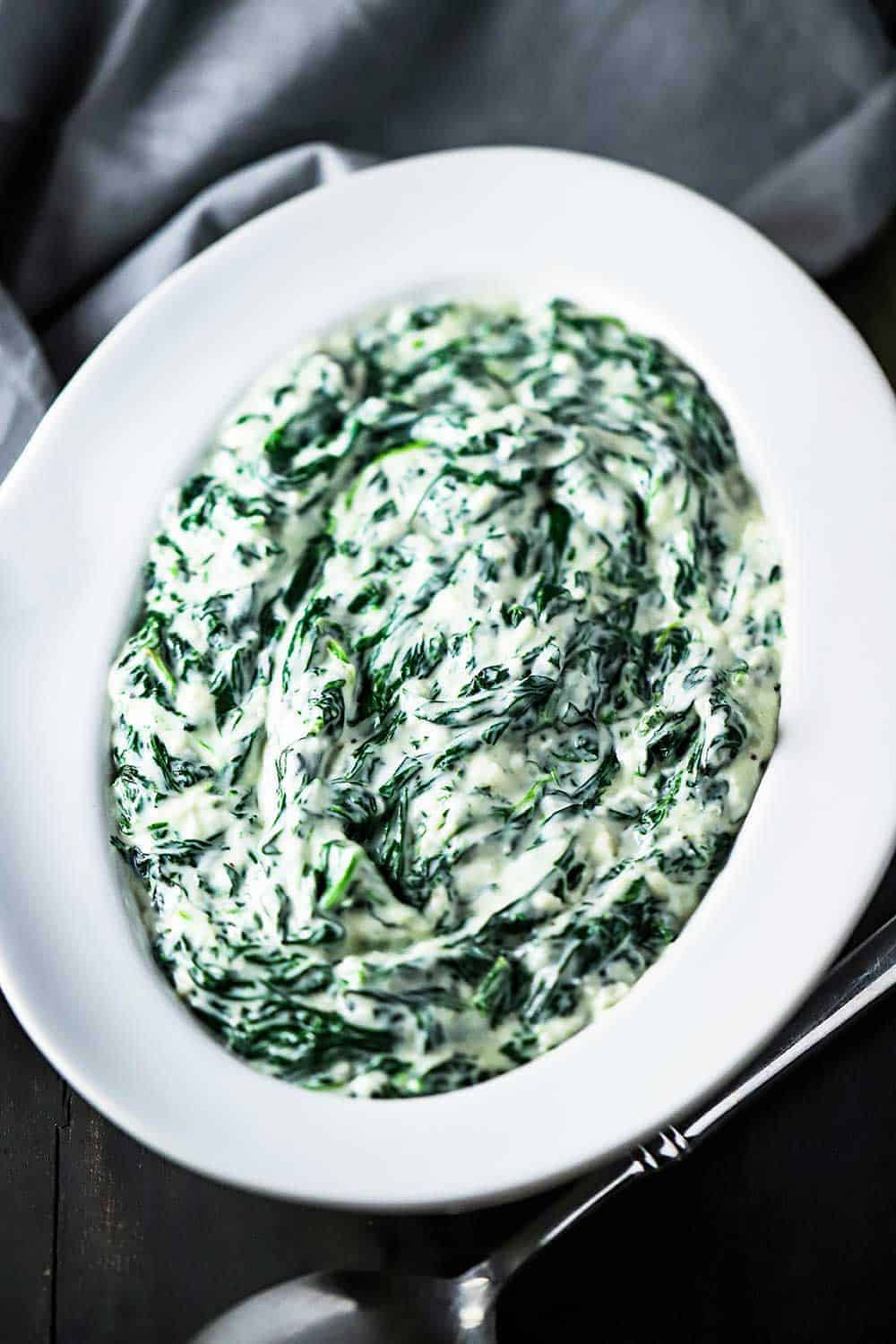 A white oval serving bowl filled with creamed spinach.