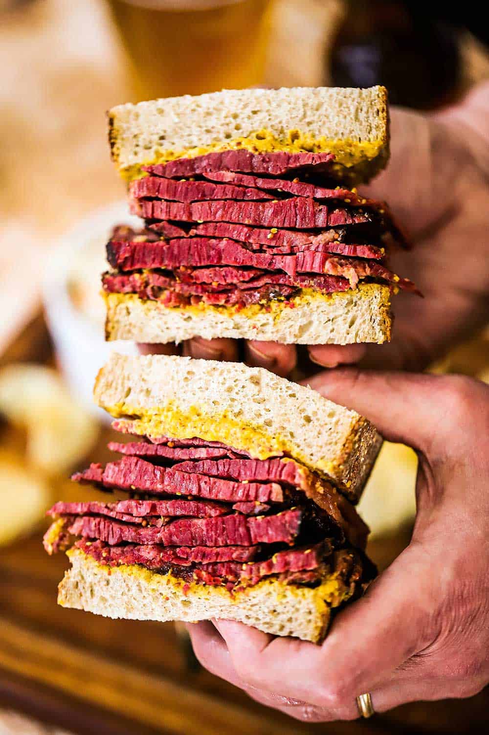 A person holding two halves of a Wagyu pastrami sandwich on rye bread. 