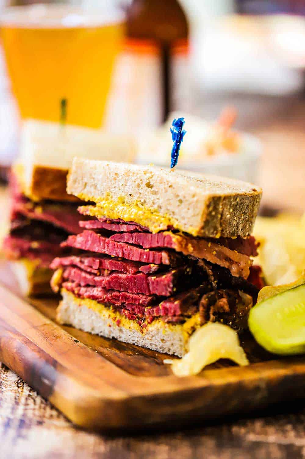 A pastrami sandwich that has been sliced into two halves both sitting a small wooden cutting board. 