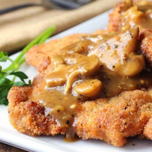 German schnitzel with mushroom gravy on a white plate next to a napkin with a silver fork