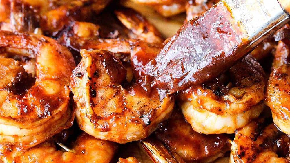 A close up view of barbecued shrimp being lathered with homemade bbq sauce. 