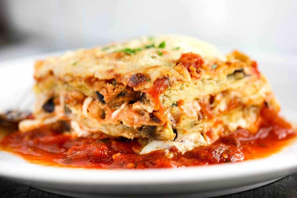 Eggplant Parmesan in a white plate with fresh marinara sauce. 