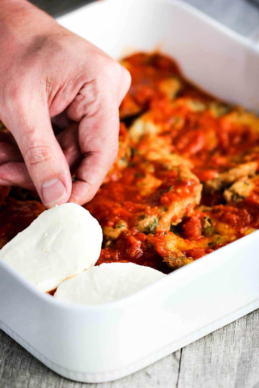 A baking dish of eggplant parmesan with layers of fresh mozzarella being layered in.