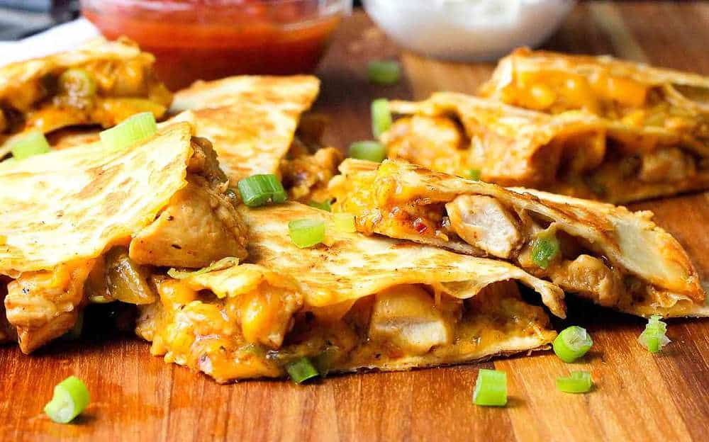 cut chicken quesadilla on a cutting board with salsa and sour cream