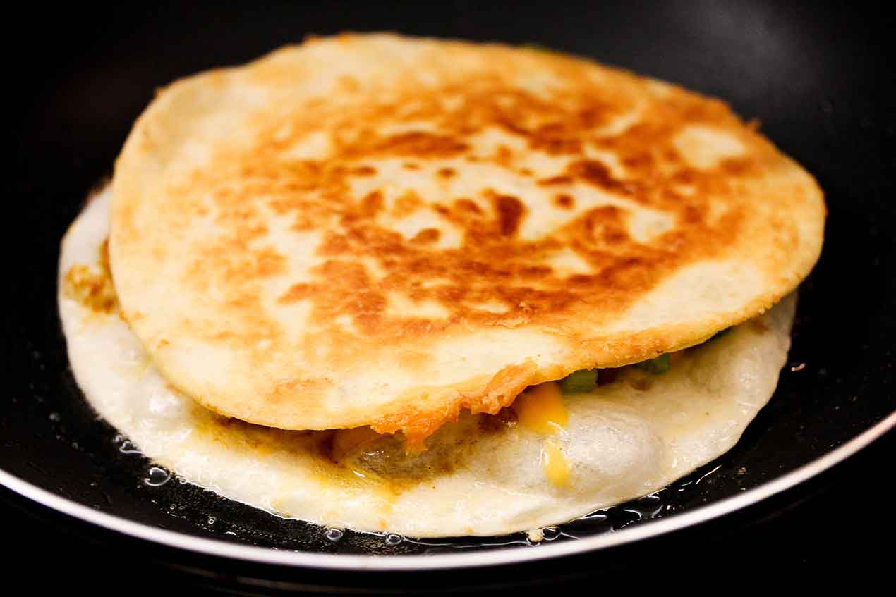 two tortillas with chicken quesadilla filling in a hot skillet