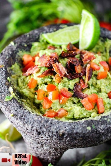 A molcajete filled with fresh guacamole topped with tomatoes and bacon