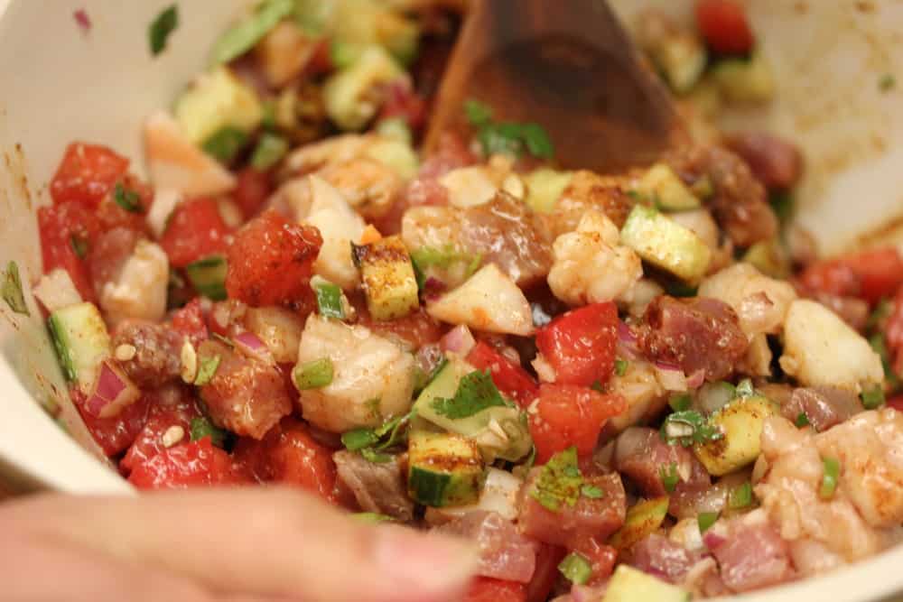 Two hands using wooden spoons to mix up ceviche. 