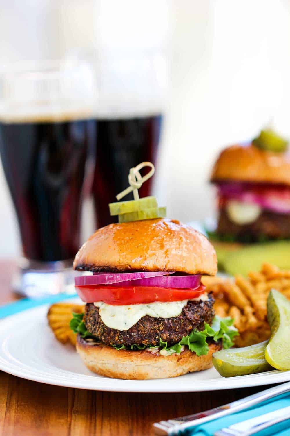 A black and bleu burger on a plate in front of two glasses of dark beer. 