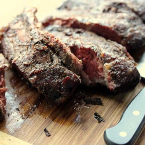 A wood cutting board with beef back ribs next to a knife.