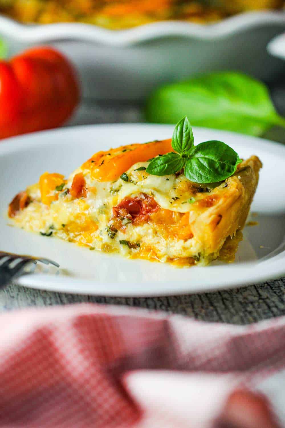 Slice Southern Tomato Pie after it cools slightly onto a white plate with a sprig of basil on top. 