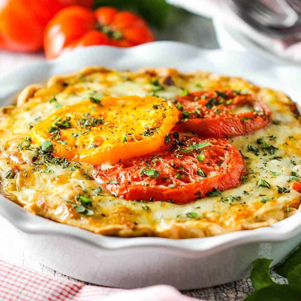 Southern Tomato Pie in a white pie dish with tomatoes nearby.