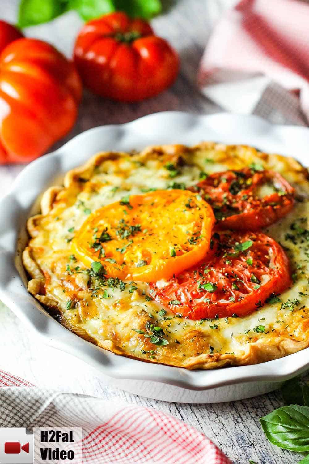 Southern tomato pie in a white pie dish with heirloom tomatoes nearby. 