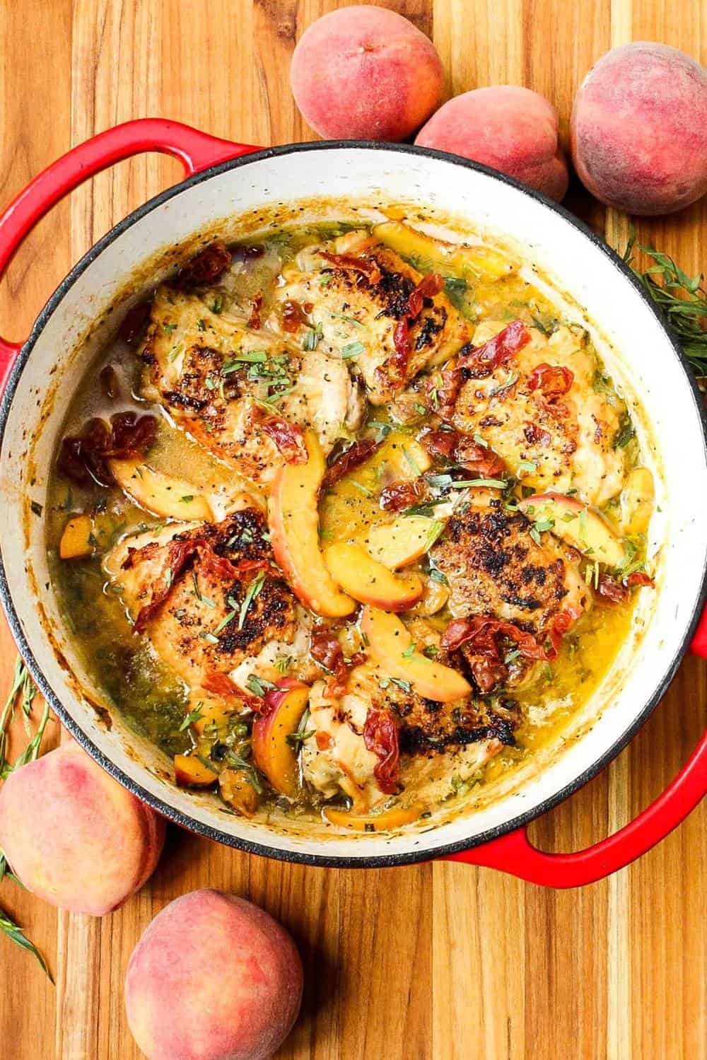 An overhead view of a pot of braised chicken with peaches on a wooden board.