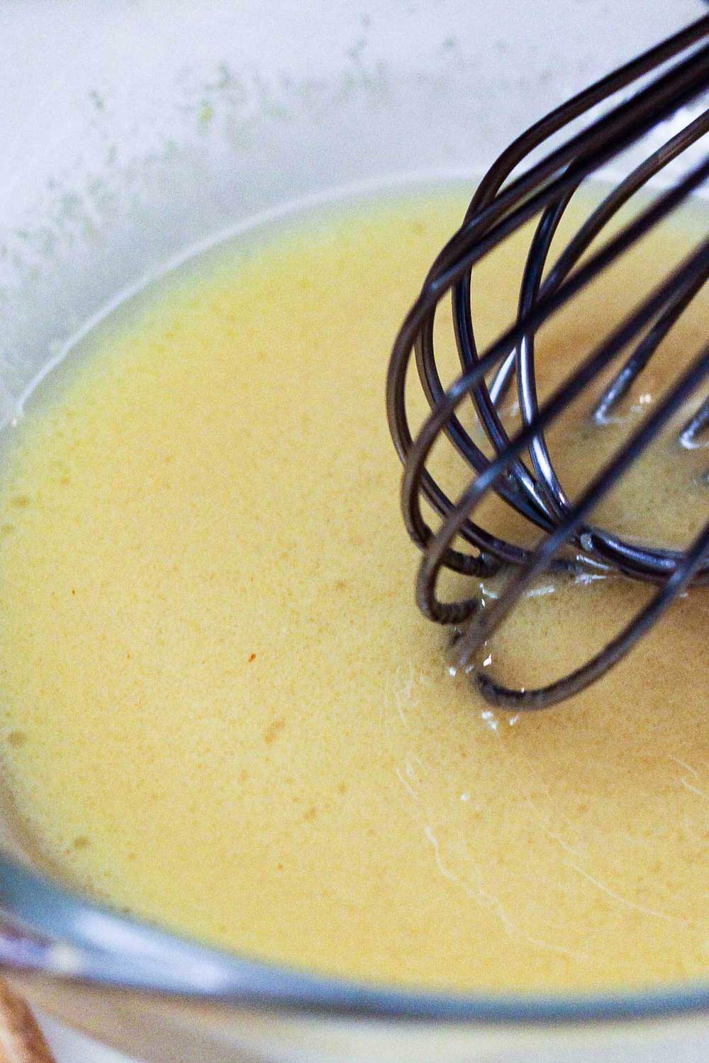 Dijon vinaigrette in a bowl being whisked with a wire whisk for cucumber and dill salad. 