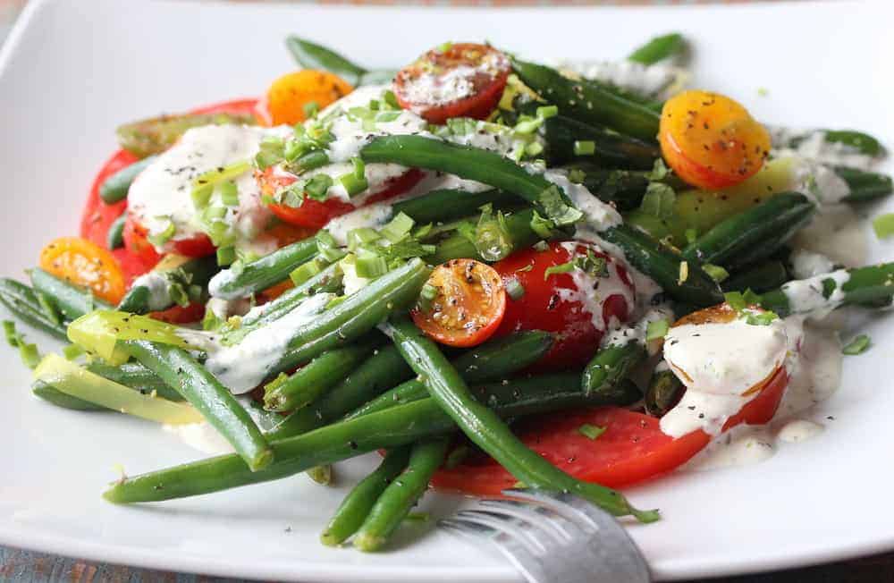Green bean and tomato salad on a white plate with a fork next to it. 