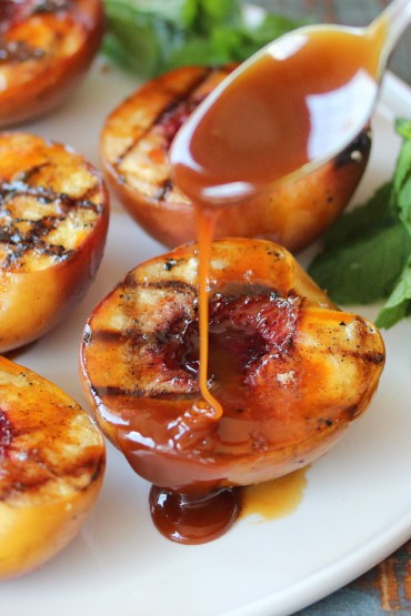 Grilled peaches on a white plate being drizzled with rum caramel sauce