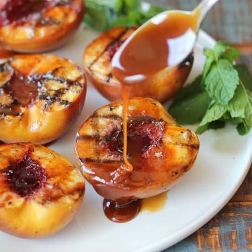 Grilled peaches on a white plate being drizzled with rum caramel sauce