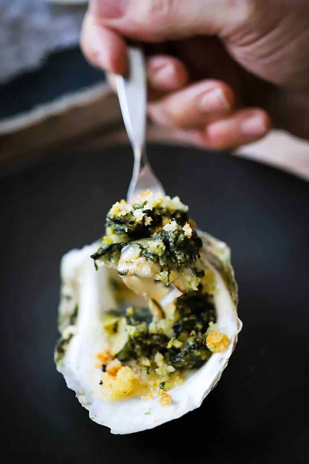 A spoon being held up with a spinach mixture in it from an oysters Rockefeller. 