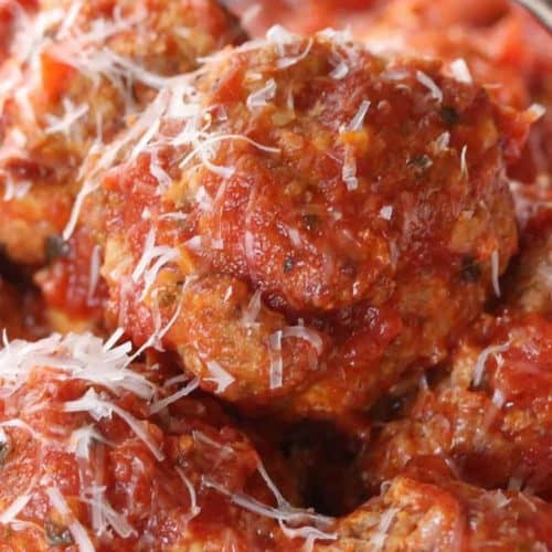 Homemade Italian meatballs with a cheese grater above grating Parmesan cheese.