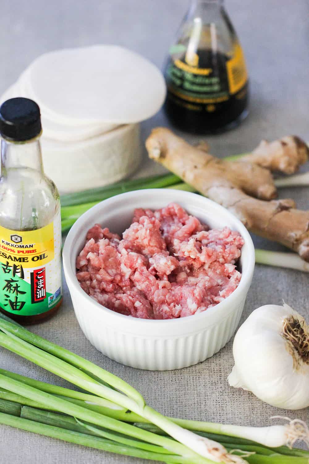 Ground pork, sesame oil, fresh garlic and ginger, an soy sauce on a grey table. 